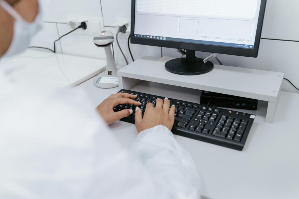 Scientist in white coat using a computer in a laboratory setting, focusing on data analysis.